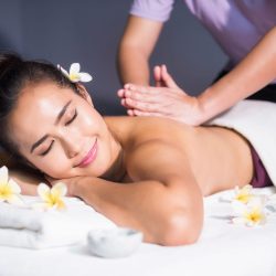 Thai oil back spiral massage to Asian woman by masseuse Thai oil back spiral massage to young Asian beautiful woman with white Plumeria on bed in spa salon. Body care treatment by masseuse. Alternative medical health care industry