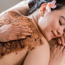 woman in spa salon having spa therapy coffee scrub Beautiful woman in spa salon having spa therapy coffee scrub procedure with hands of masseur