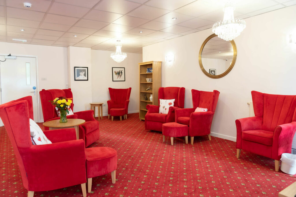 Lounging area with red chairs, foot stools and carpet.
