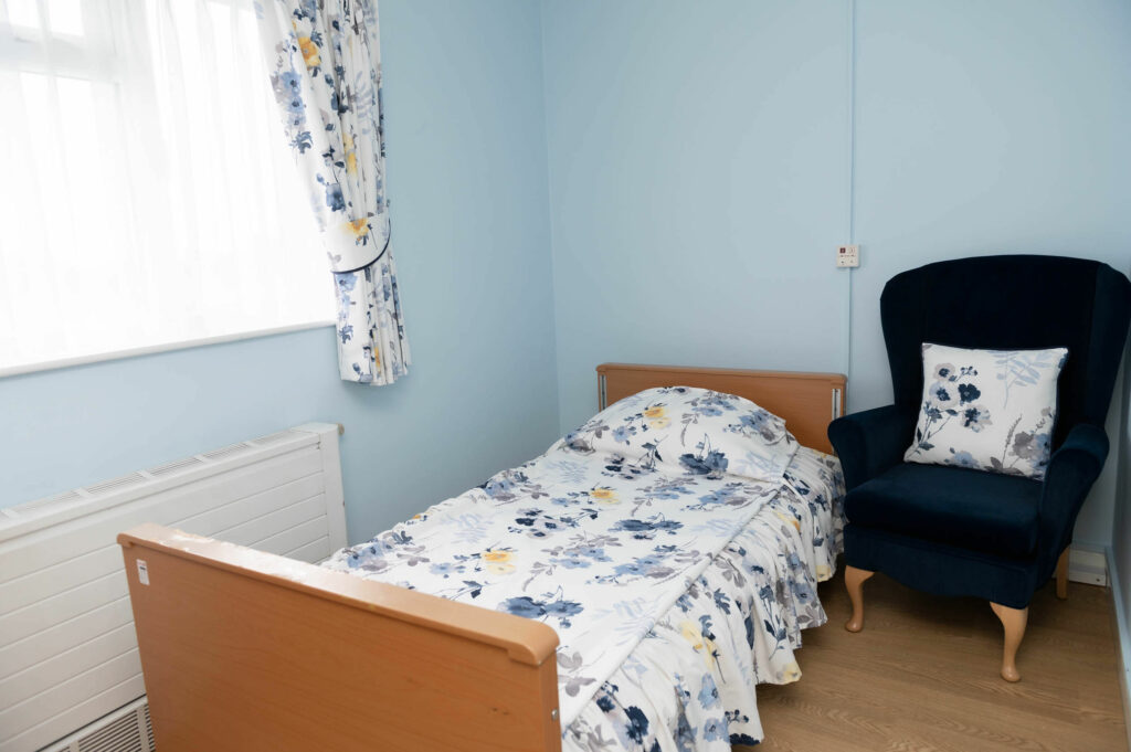 Single bedroom with a window and radiator to the left of the bed and dark coloured arm chair to the right.