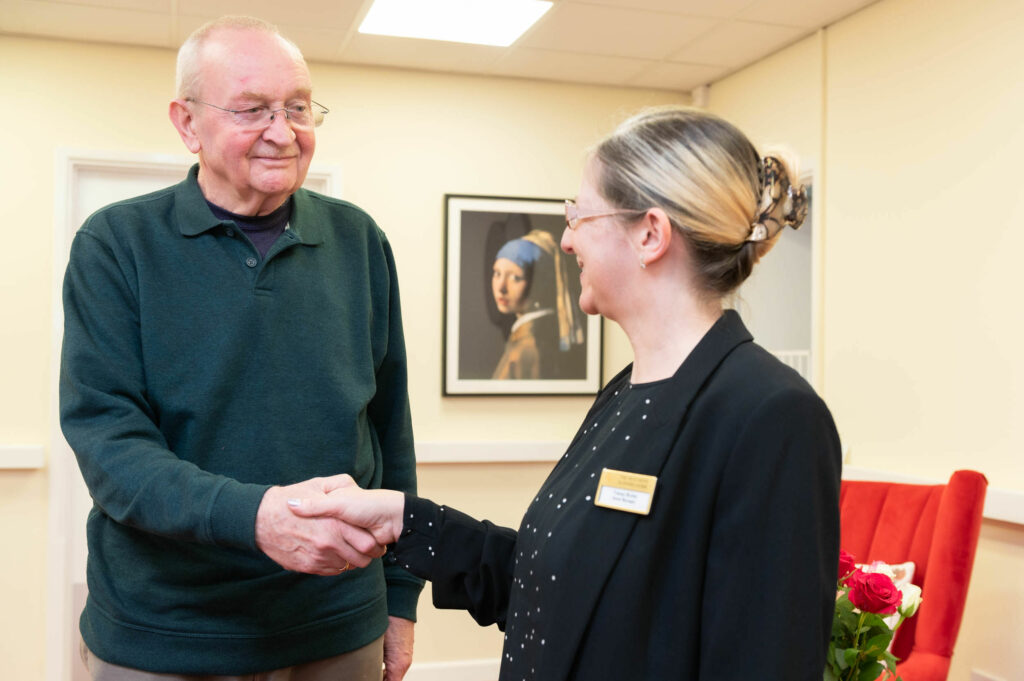 An elderly resident shaking hands with a member of staff.