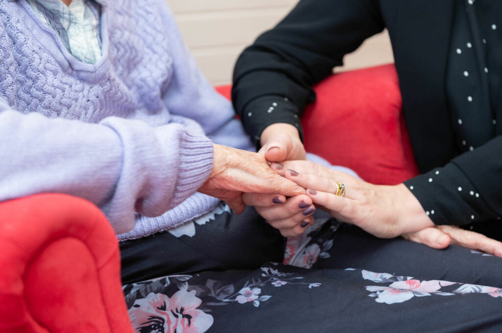 An elderly resident holding hands with a member of staff.