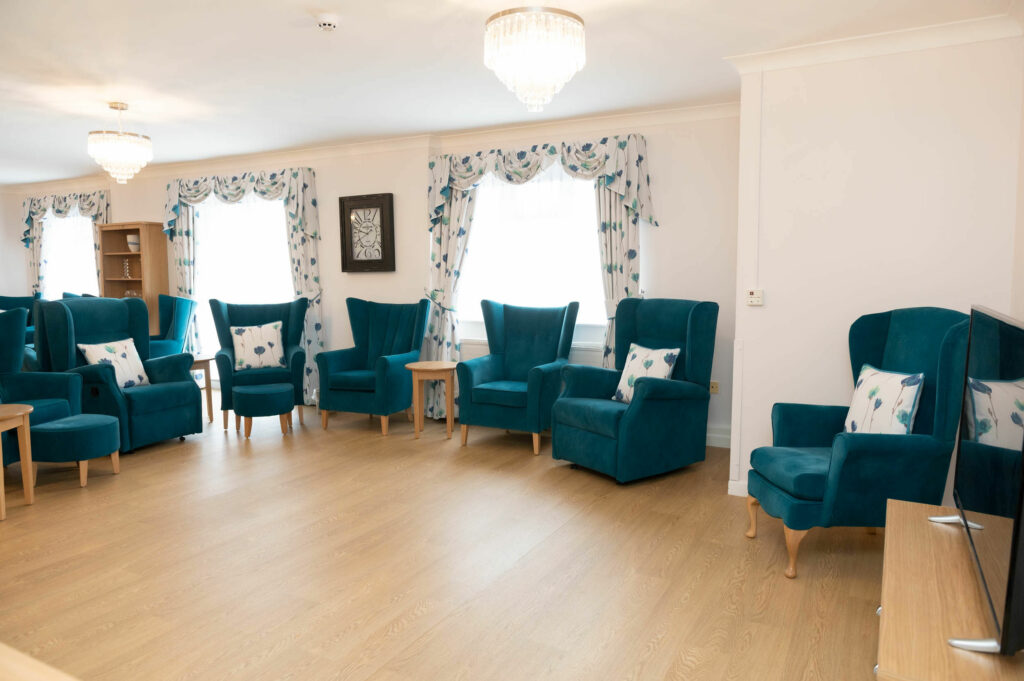 Lounging area with blue chairs and foot stools and wooden tables.