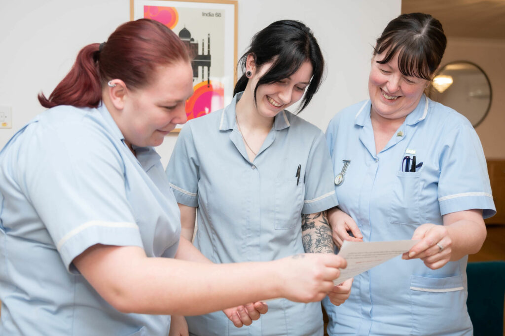 3 members of staff smiling whilst looking at a piece of paper together.