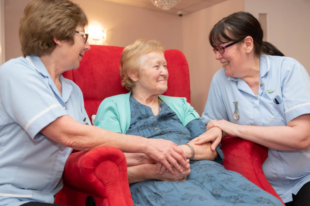 2 members of staff holding hands with an elderly resident.