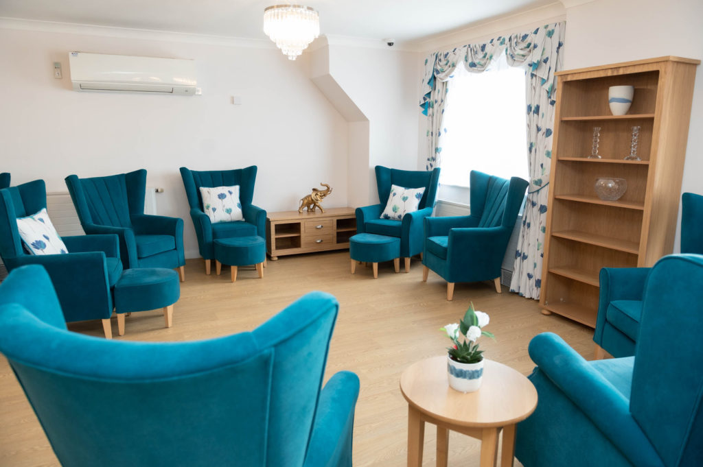Lounging area with blue chairs and foot stools and wooden tables.
