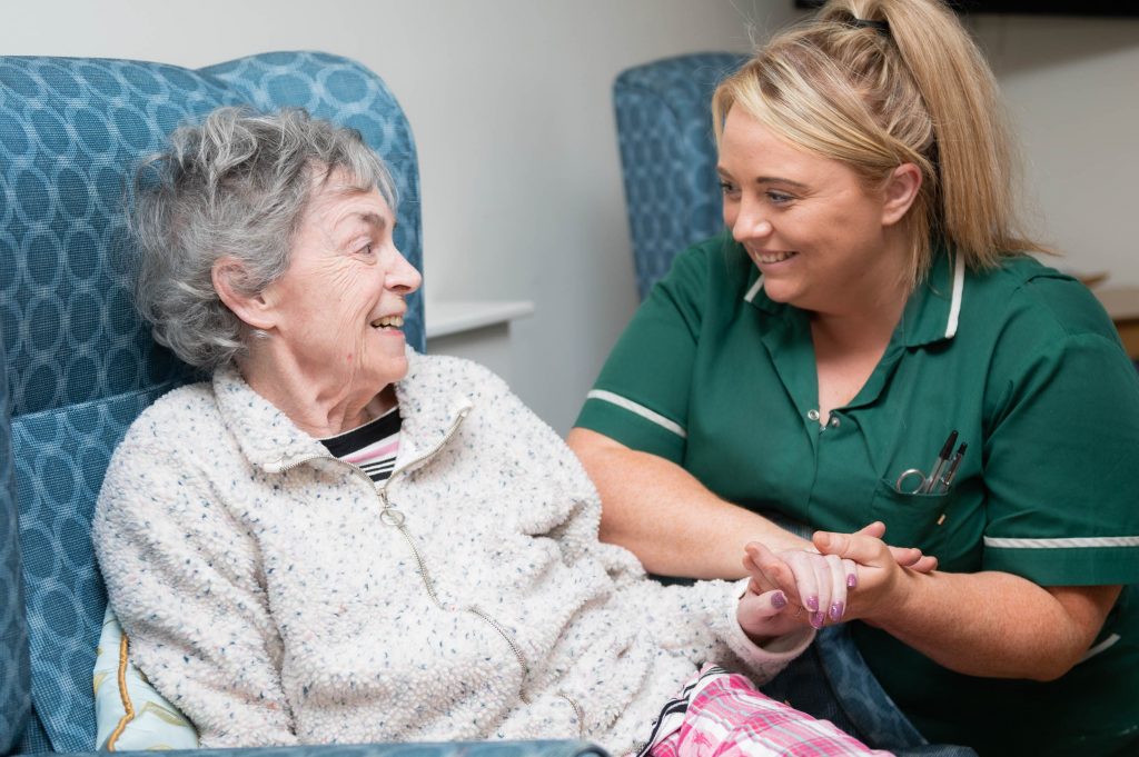 Elderly resident holding the hand of a member of staff, they are both smiling.