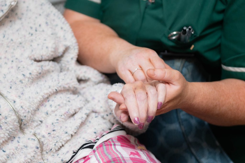 Elderly resident holding the hand of a member of staff