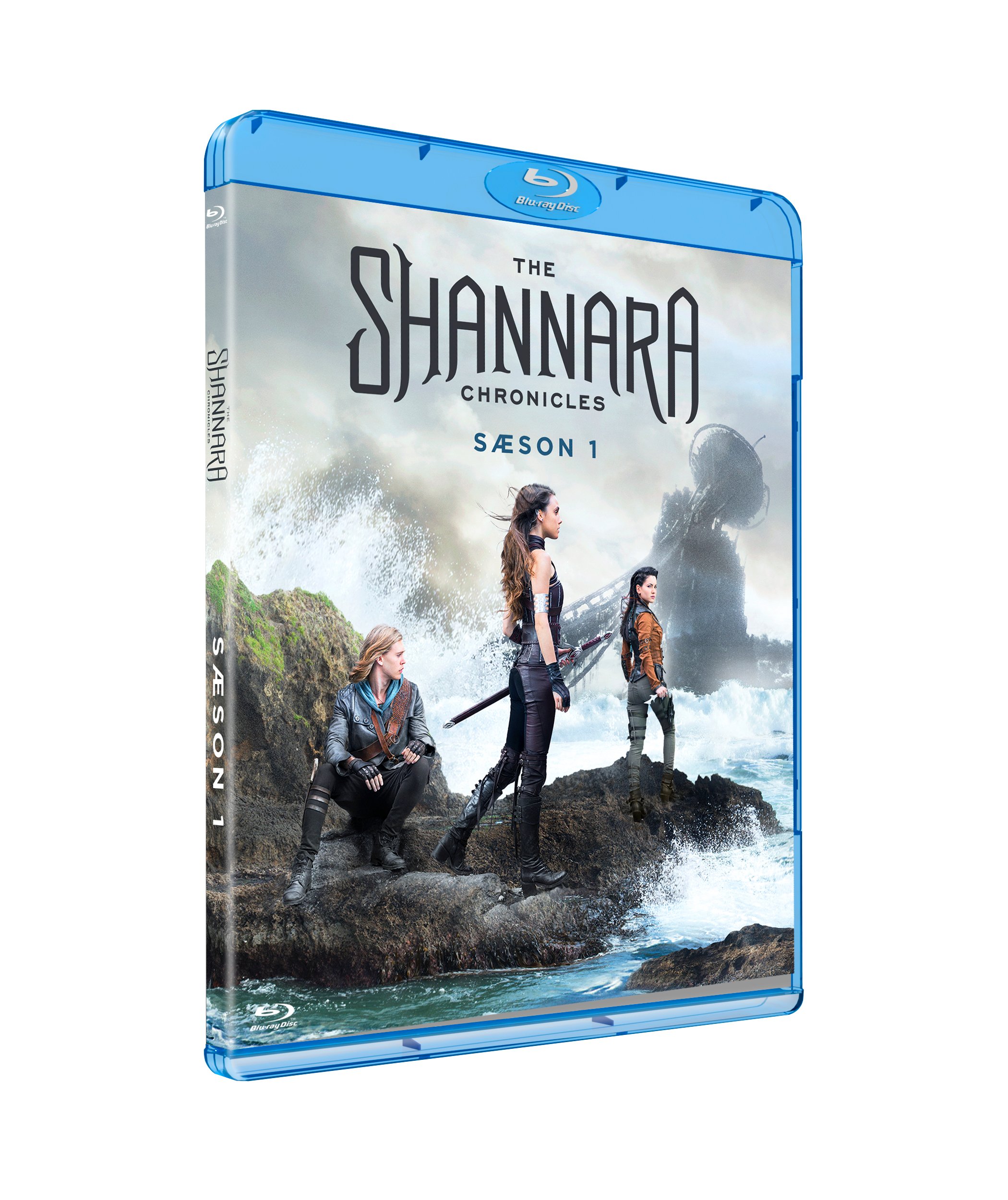Blu-ray-omslag til The Shannara Chronicles: Season 1 med tre karakterer, der står på et klippeterræn ved havet med bølgeskvulp og en stor, fjern statue i baggrunden.