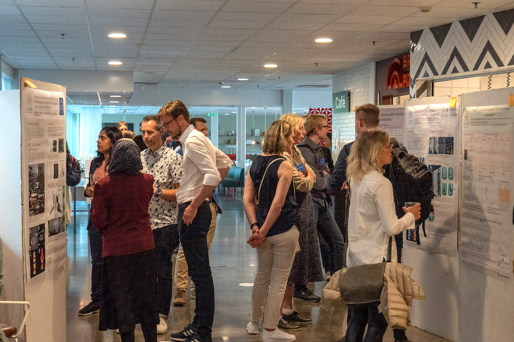 Människor står och diskuterar framför skärmar med postrar