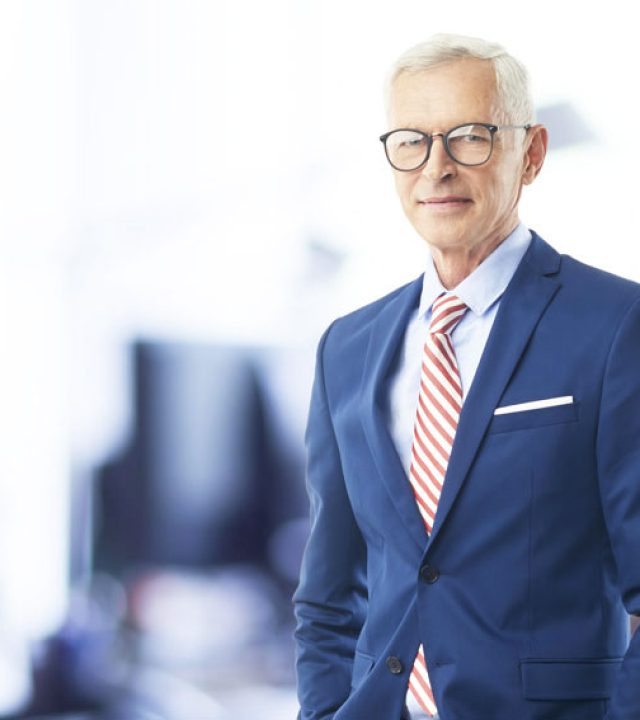 A senior sales director businessman looking at camera and smiling while standing at the office.