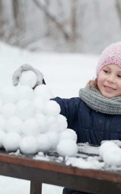Child girl playing with snowballs on a walk in winter snowy park