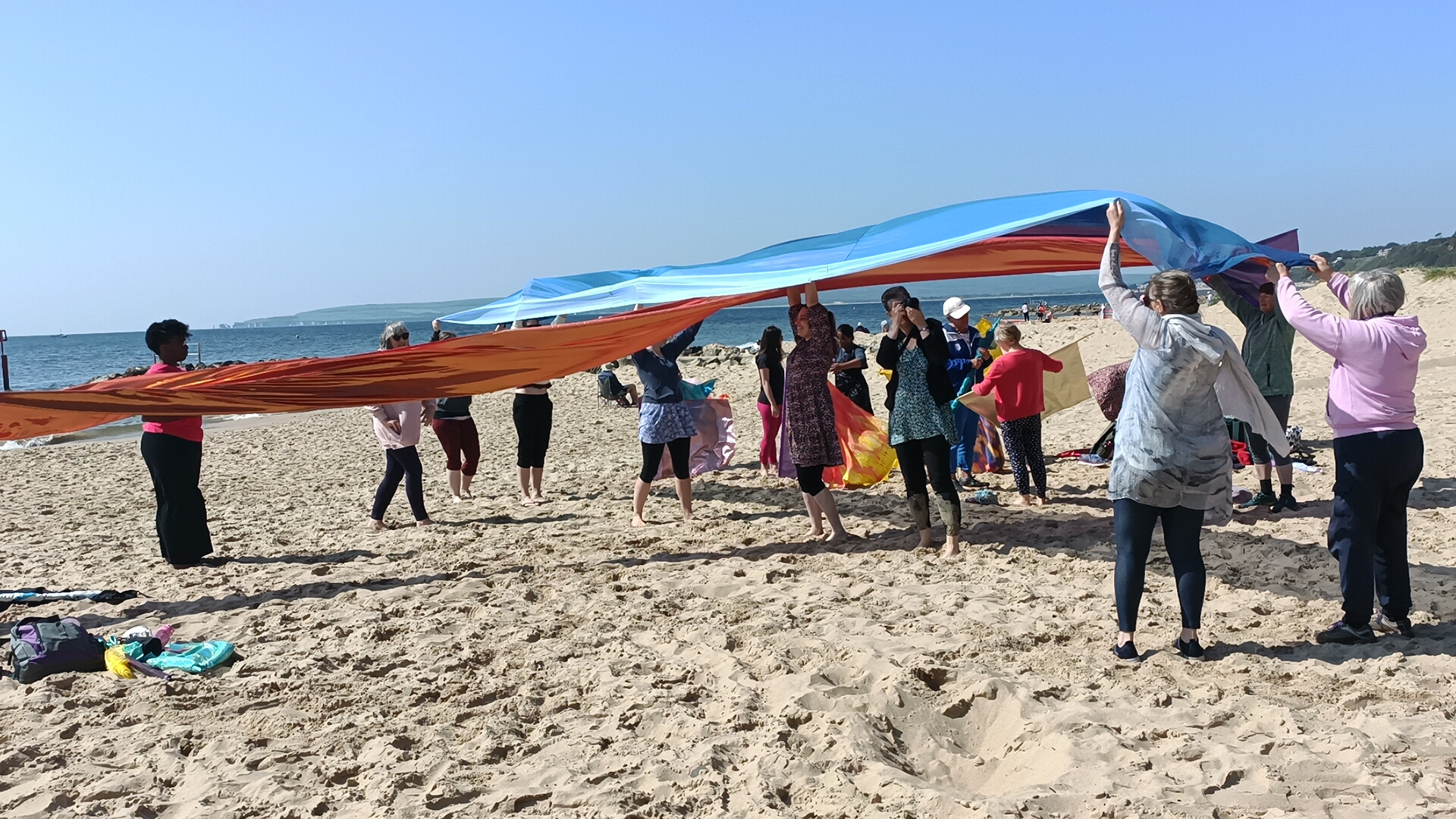 Orange and blue cross with people under it on sand