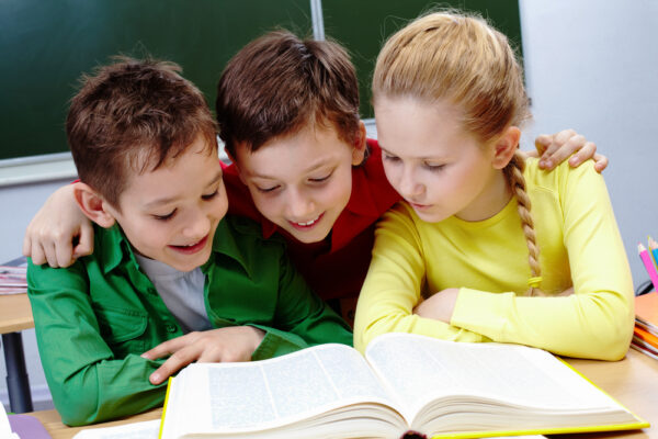 Reference: Øget kundskab i skolen. Tre børn læser i en bog