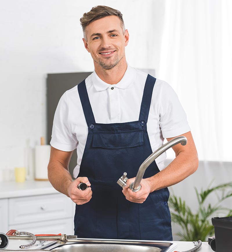 Vaktmästare står i kök och fixar kran i diskho