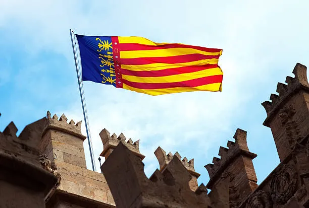 Valencian flag waving above crenellated stone towers under a blue sky
