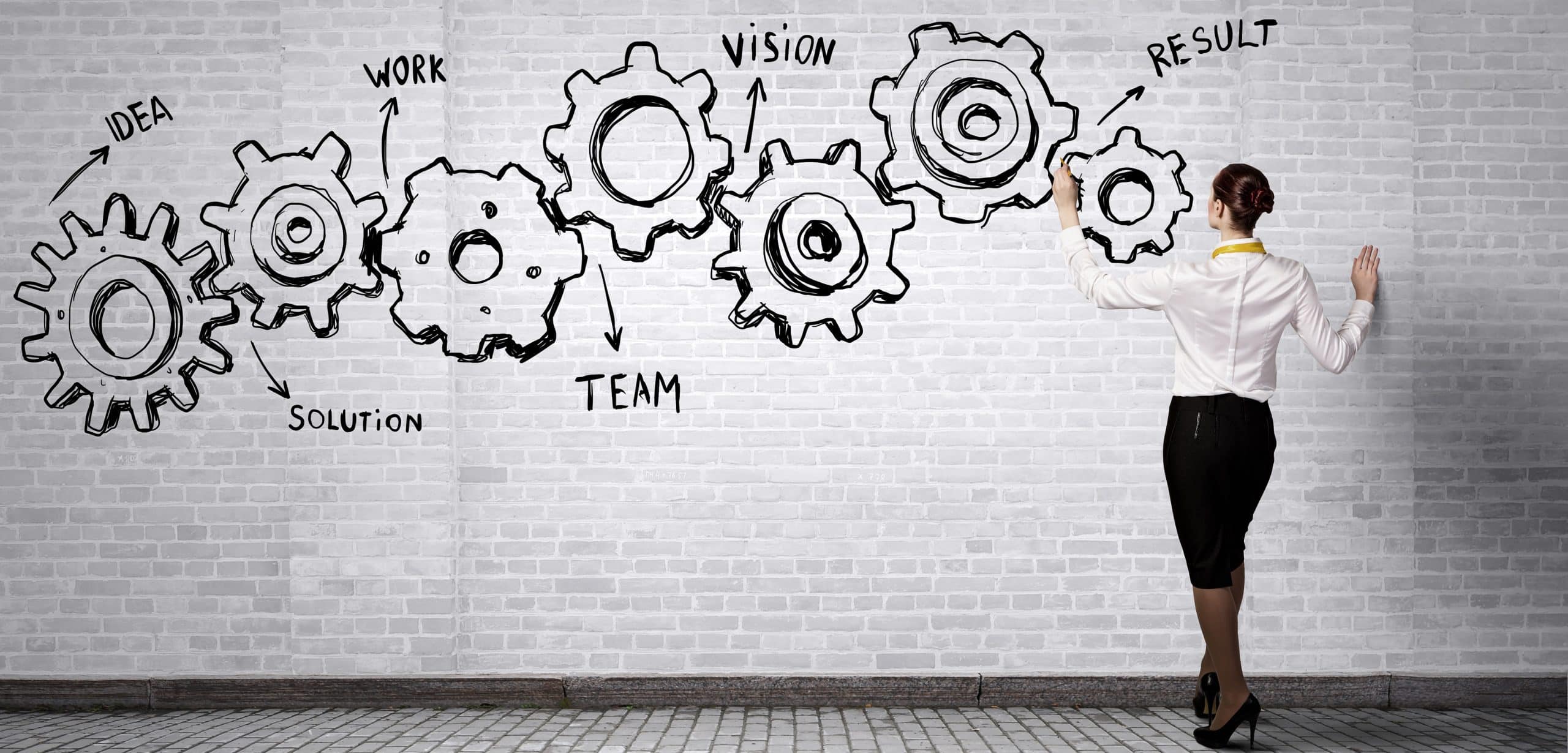 Young business woman drawing gears on a wall for illustrating the process from idea to final result