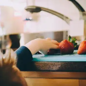 ett barn som str&auml;cker sig efter en jordgubbe p&aring; en b&auml;nk