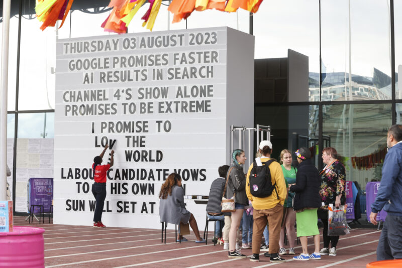 In front of a giant marquee board, someone writes out, using plastic letters: I promise to love the world.