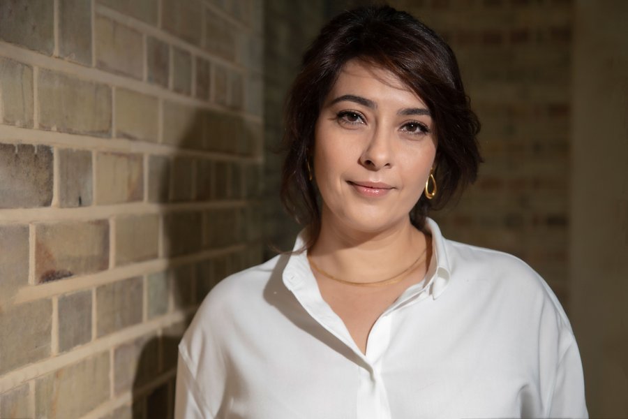 Female-presenting person stood infant of a brick wall.