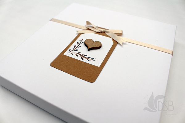 White box containing wedding invitations. A nude ribbon ties it together with a tag.