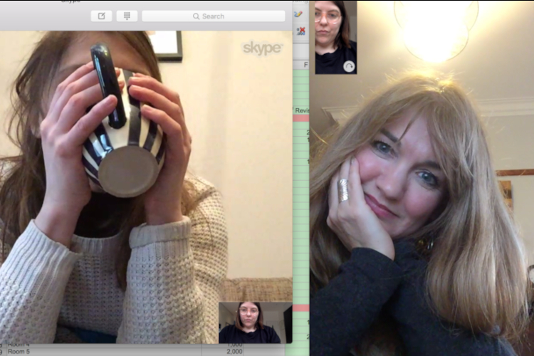 A screengrab of two concurrent video calls. On the right a blond haired white woman smiles while cupping her face in her hand. On the left a dark haired white woman's face is obscured by the mug she is drinking from. Tiny windows in each image show a third white woman.