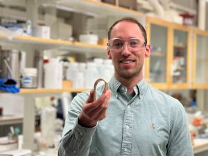 A man standing in a lab is holding a curved material sample for the camera