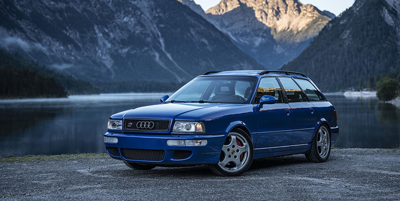 Audi RS2 (bilden nedanför), som lanserades 1994, var den första modellen i RS-serien av högpresterande bilar. Den var delvis utvecklad av Porsche och tillverkad i samarbete med dem. RS2 delar flera komponenter och designelement med Porsche-modeller av den tiden, inklusive bromsar, grill, fälgar och backspeglar. Dessutom hade RS2 en motor som var gemensamt utvecklad av de två biltillverkarna. Det var ett framgångsrikt samarbete som lade grunden för RS-serien av prestandabilar.