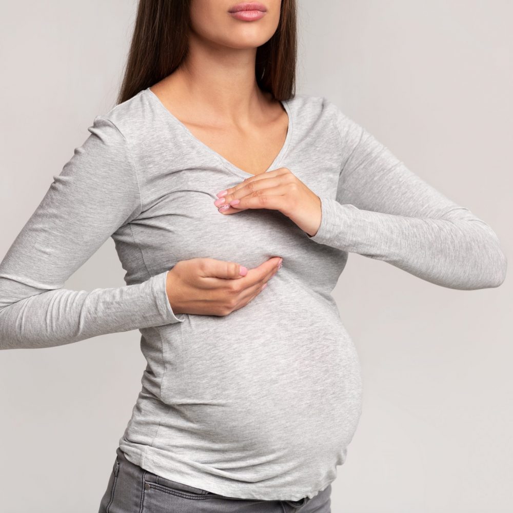 Unrecognizable Pregnant Lady Suffering From Breast Pain Standing, Gray Background Sore Breasts. Unrecognizable Pregnant Lady Suffering From Pain Touching Chest Standing Over Gray Studio Background. Cropped