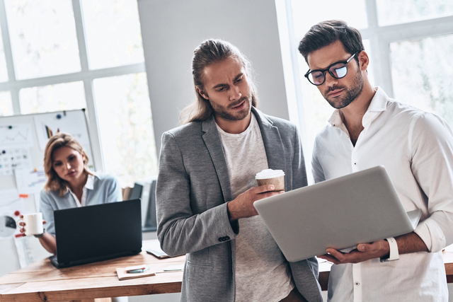 Working as a team. Two young modern men in smart casual wear using laptop while working in the creative office