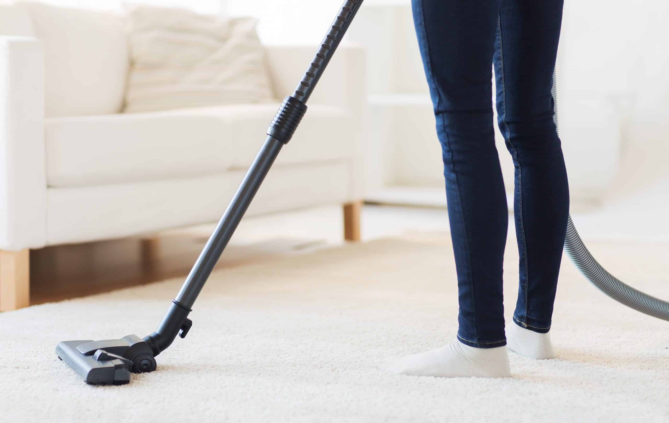 people, housework and housekeeping concept - close up of woman with legs vacuum cleaner cleaning carpet at home