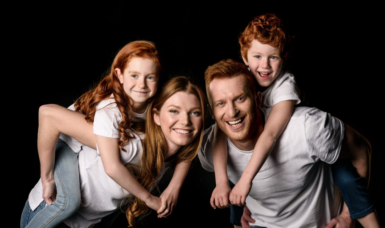 Happy redhead family in white t-shirts smiling isolated on black