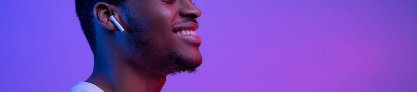 Relaxed African American Man Listening Music In Wireless Airpods Earphones In Neon Light, Smiling Black Guy Wearing Bluetooth Earpods Enjoying Favorite Songs Over Purple Background, Panorama