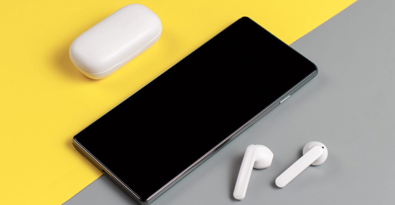 Smartphone and white wireless earphones with the case top view on grey and yellow background