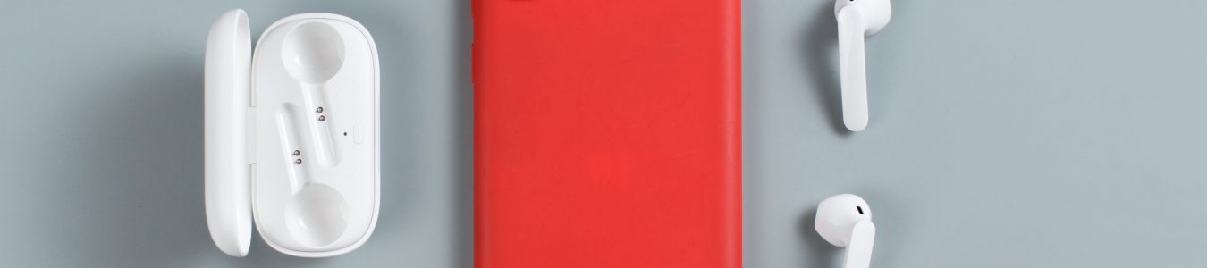 Smartphone with red cover and white wireless earphones top view on grey background