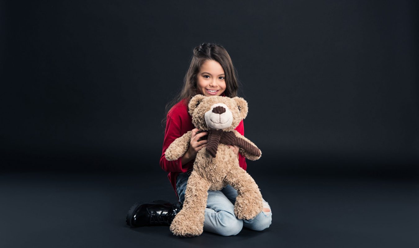 Smiling kid holding teddy bear isolated on black