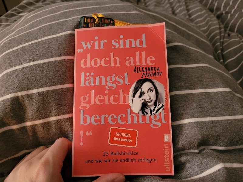 Buch auf Bettdecke - Buchtitel: Wir sind doch alle längst gleichberechtigt - 25 Bullshitsätze und wie wir sie endlich auseinander nehemen"