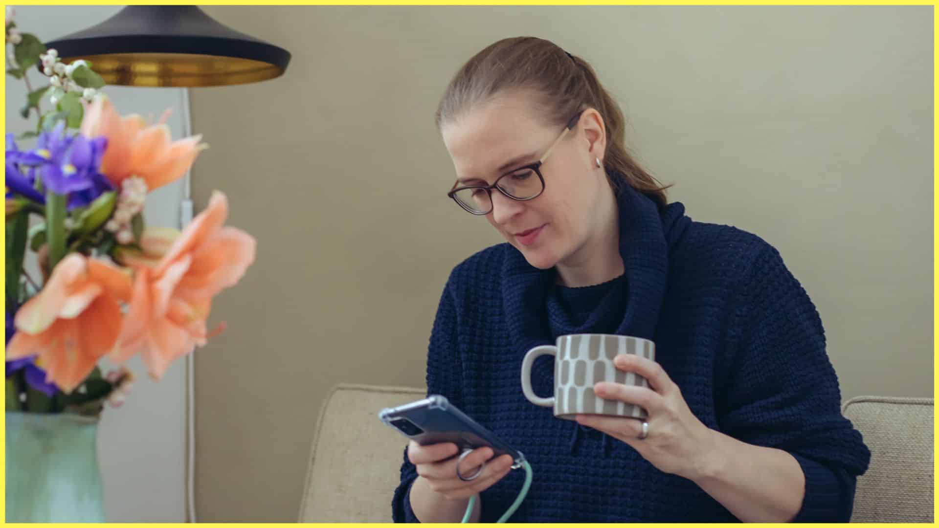 Eine Frau hält eine Kaffeetasse und schaut nachdenklich auf ihr Handy, es soll den Titel unterstreichen, dass wir mehr über unsere Körpermitte sprechen soll, online und offline.