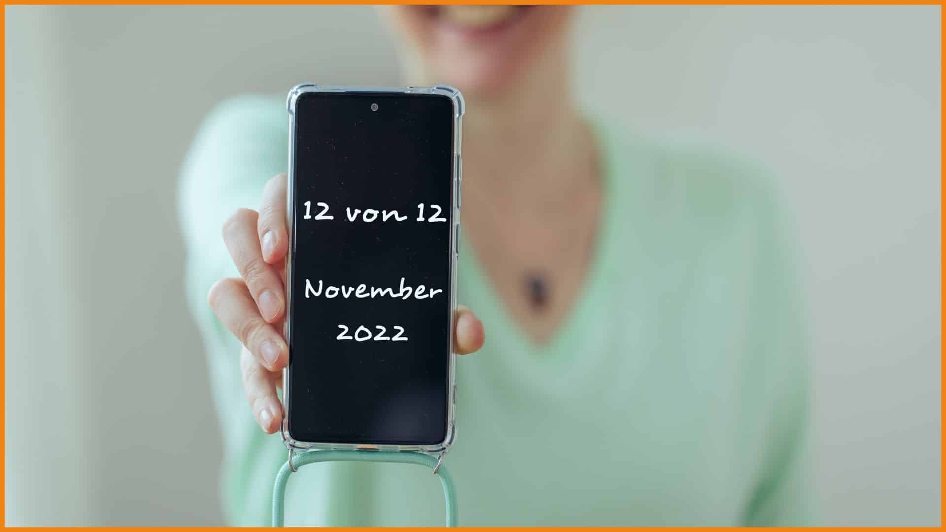 Ein unscharfer Oberkörper mit ausgestrecktem Arm. In der Hand vorne wird ein Handy mit schwarzem Bildschirm gehalten. In Schreibschrift ist darauf eingefügt: 12 von 12 November 2022