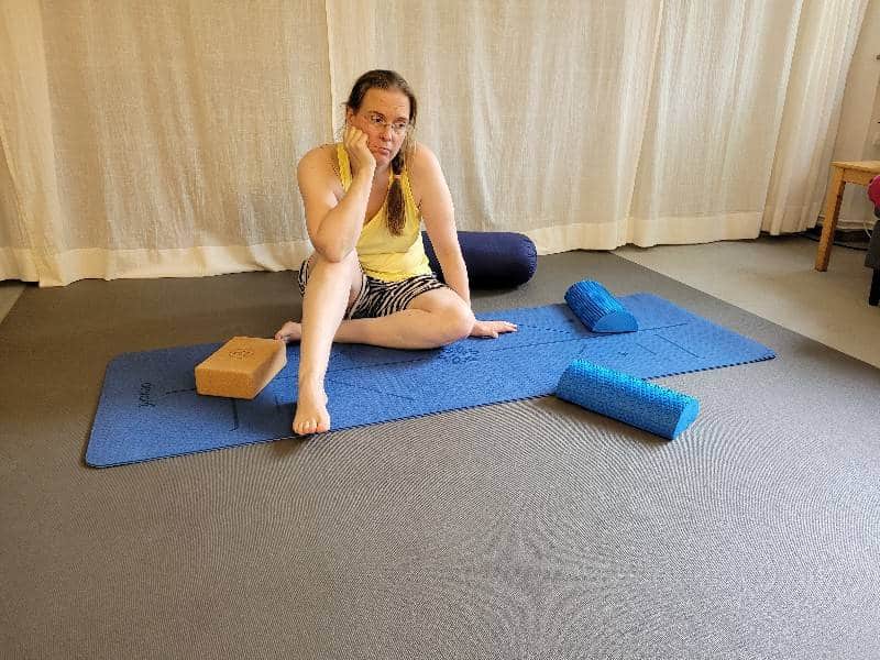 Eine Frau in Sportklamotten sitzt auf einer Yogamatte. Sie stützt ihr Gesicht in eine Hand auf und guckt unzufrieden.