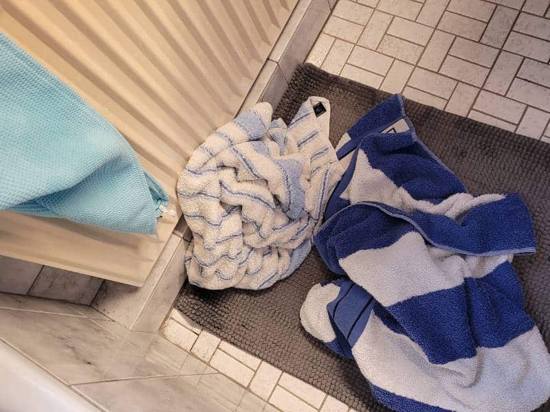 Zwei Handtücher, die auf dem Badezimmerfußboden liegen und eines, was über der Heizung hängt.