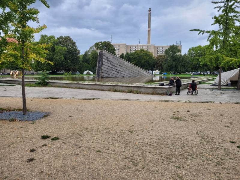 Blick auf ein Denkmal der Berliner Mauer: ein Stück Mauer versinkt schief in einem Brunnen.