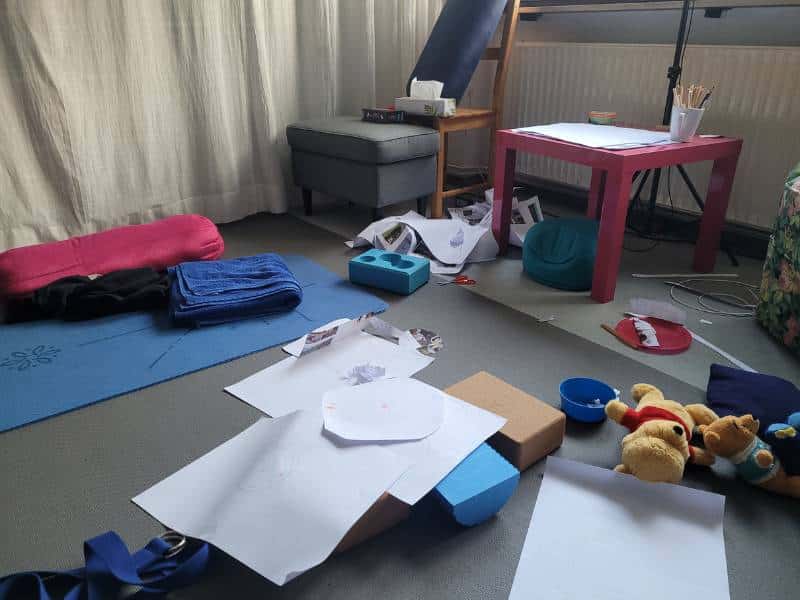 Blick auf meine Arbeitsecke mit YOgamatte und anderen Arbeitsutensilien. Darüber verteilt liegen Kuscheltiere, Malkrams und Malblätter vom Kind verteilt. Es ist sehr chaotisch.