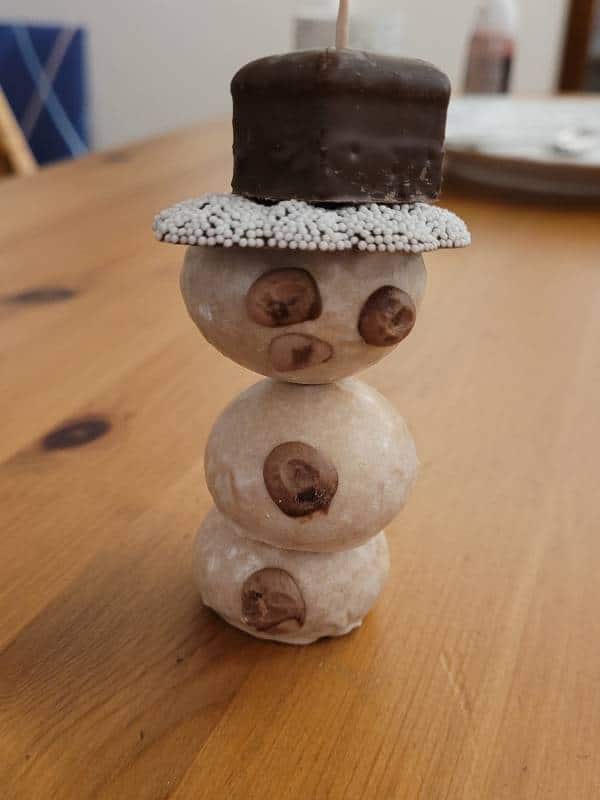 Ein essbarer Schneemann, gebastelt aus drei Pfeffernüssen, einem Kringel und einem Dominostein.