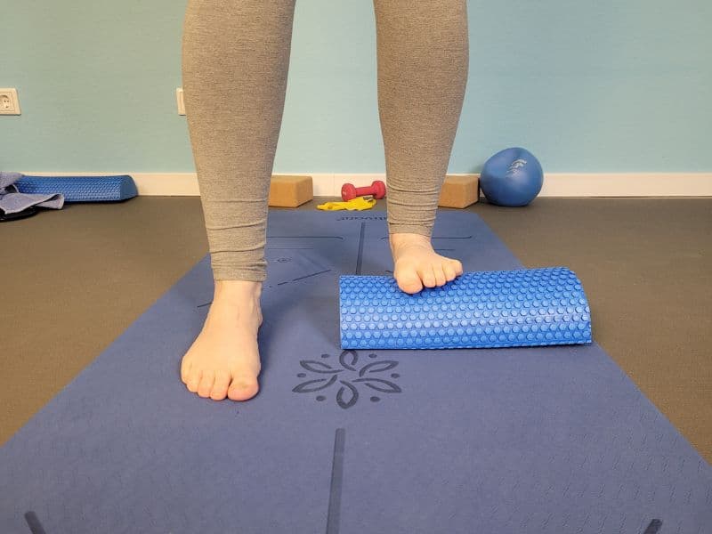 Man sieht zwei nackte Füße von vorne, die Beine sind in Leggins. Ein Fuß steht auf einer Halbrolle, um auf dieser Seite eine Wadendehnung zu erzielen.