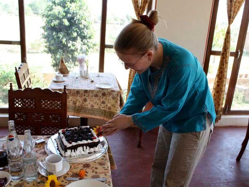 Eine Frau in beiger Leinenhose und luftigem, aber langärmeligem türkisen Leinenshirt schneidet einen Kuchen an