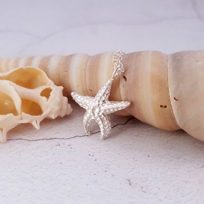 Sterling silver starfish pendant draped over a shell made by Aimee Winstone Jewellery in Bristol