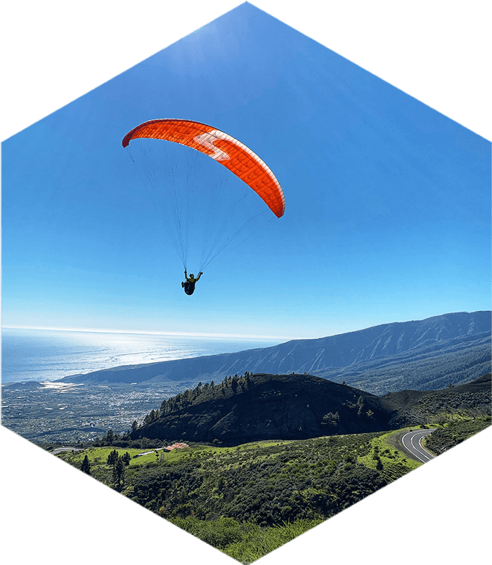 Solo paraglider with red wing flying over green mountain scenery