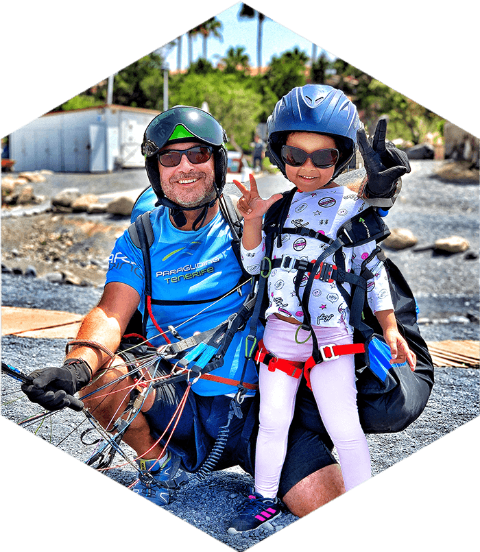 paraglider and small child on the ground giving peace signs