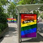 Pride colored poster at a bus stop in Paris with the text "Cause we're living in a world of fools, breaking us down, when they all should let us be. #LoveIsLove"